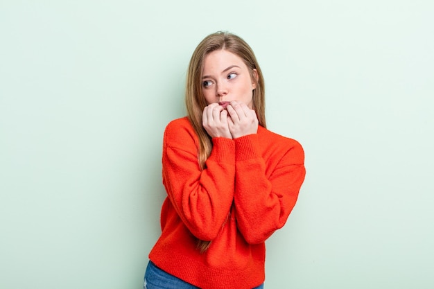 Blanke roodharige vrouw die er bezorgd, angstig, gestrest en bang uitziet, vingernagels bijt en op zoek is naar zijdelingse kopieerruimte