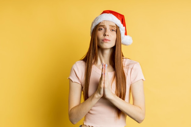 Blanke roodharige vrouw met sproeten die een gebedsgebaar maakt, de handpalmen bij elkaar houdt, de vriend met een smekende blik vraagt om haar droom te vervullen, om een cadeau op een gele achtergrond te kopen. Lichaamstaal concept.