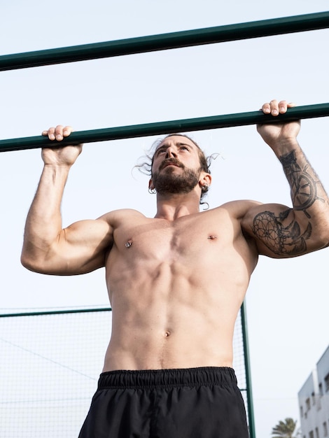 Blanke shirtloze man doet pull-ups buiten in het openbare park