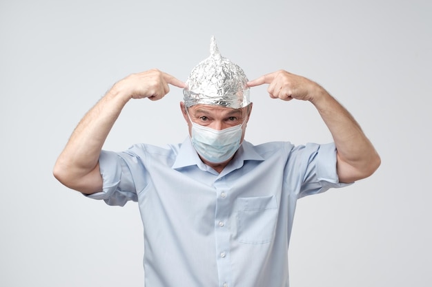 Blanke volwassen man met een hoed van aluminiumfolie en een medische hoed die zich niet graag verbergt voor het buitenleven