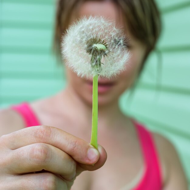 Blanke vrouw bedekt haar gezicht met een paardenbloem en probeert niet te ademen