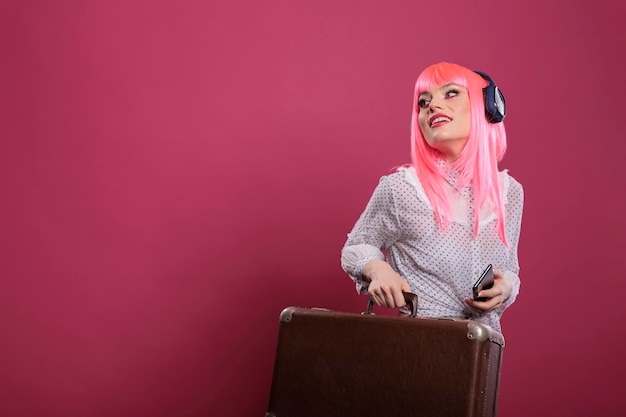 Blanke vrouw die een reiskoffer draagt om op vakantiereis te vertrekken, met een koptelefoon op. Aktetasbagage vasthouden om op stadsavontuur te gaan, reizen op stadsvakantiereis.