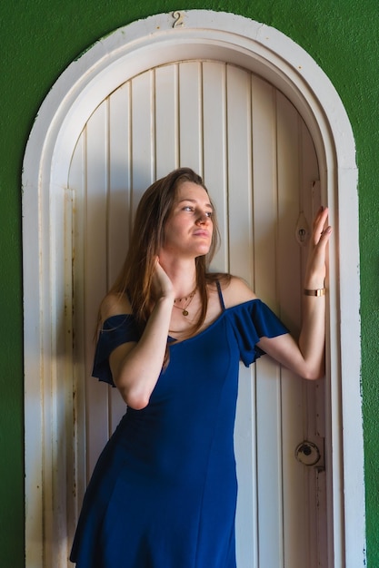 Blanke vrouw die lacht in een blauwe jurk naast een witte verkoop van een groen huis