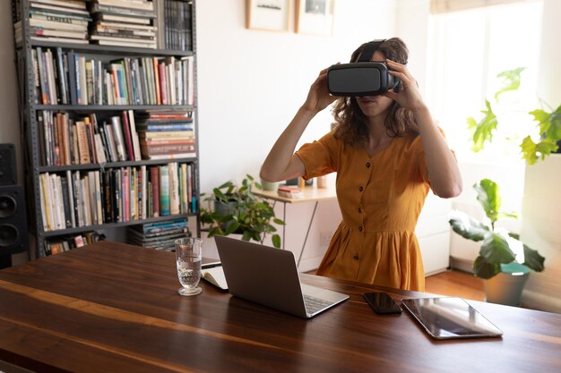 Foto blanke vrouw die tijd thuis doorbrengt, zichzelf isoleert en sociale afstand neemt tijdens quarantaine-afsluiting tijdens de coronavirus covid 19-epidemie, zittend aan een bureau met een vr-bril