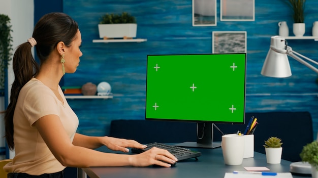 Blanke vrouw die werkt op een krachtige computer met een mock-up groen scherm chroma key zittend op een bureau. Freelancer die informatie zoekt voor zakelijk project met behulp van geïsoleerde pc