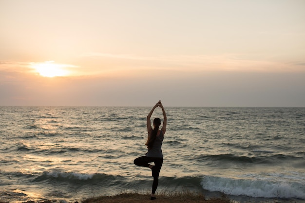 Blanke vrouw die yoga beoefent aan de kust van de oceaan