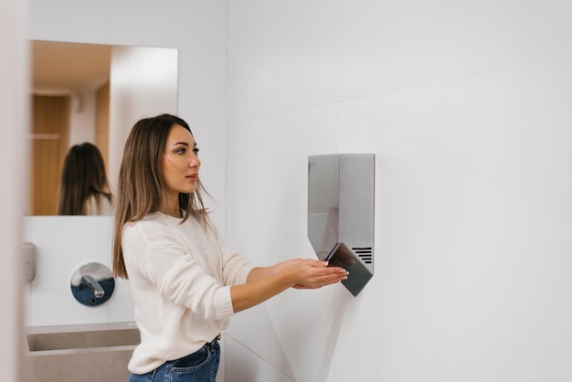 Foto blanke vrouw droogt haar handen met heet water met behulp van een droger