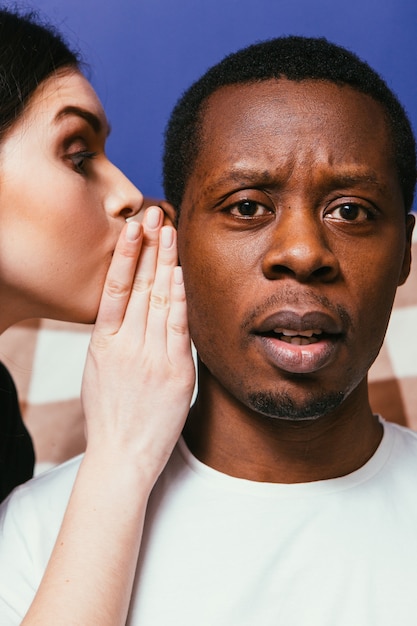 Blanke vrouw fluistert op oor naar zwarte man, close-up