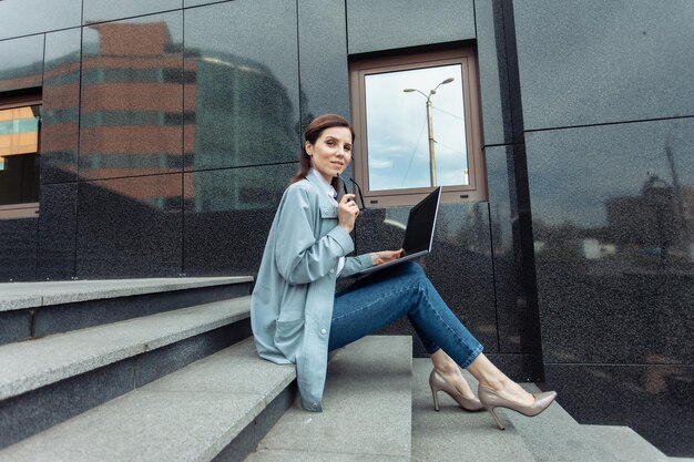 Blanke vrouw gebruikt laptop terwijl ze buiten op de trap zit Werk op afstand Moderne zakenvrouw Gebruikt gadgets Lifestyle