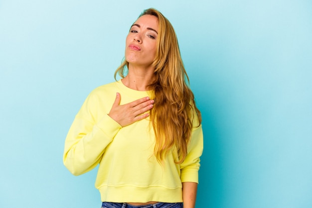 Blanke vrouw geïsoleerd op blauwe achtergrond die een eed aflegt, hand op de borst.