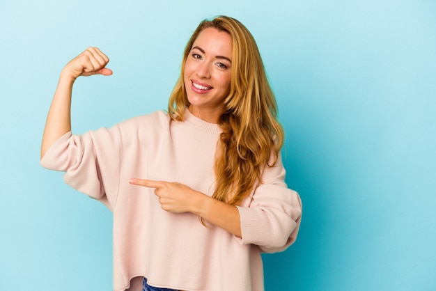 Blanke vrouw geïsoleerd op blauwe achtergrond met krachtgebaar met armen, symbool van vrouwelijke kracht