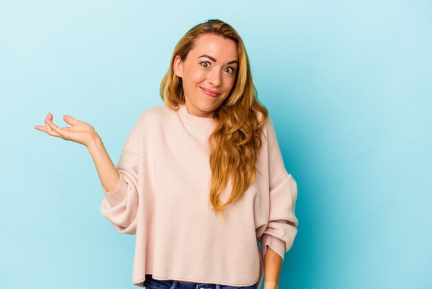 Blanke vrouw geïsoleerd op blauwe achtergrond twijfelend en schouders ophalend in vragend gebaar.