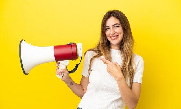 Blanke vrouw geïsoleerd op een gele achtergrond met een megafoon en wijzende kant