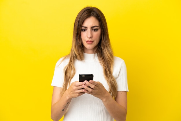 Blanke vrouw geïsoleerd op gele achtergrond met behulp van mobiele telefoon