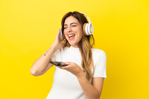 Blanke vrouw geïsoleerd op gele achtergrond muziek luisteren met een mobiel en zingen