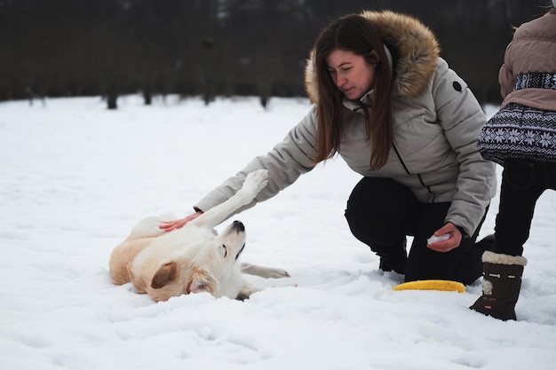 Blanke vrouw heeft haar pluizige hond in de sneeuw gegooid en krabt buik met de hand