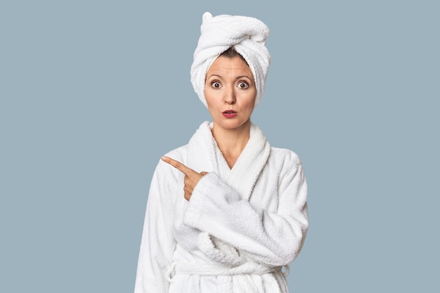 blanke vrouw in badjas en handdoek die naar de zijkant wijst