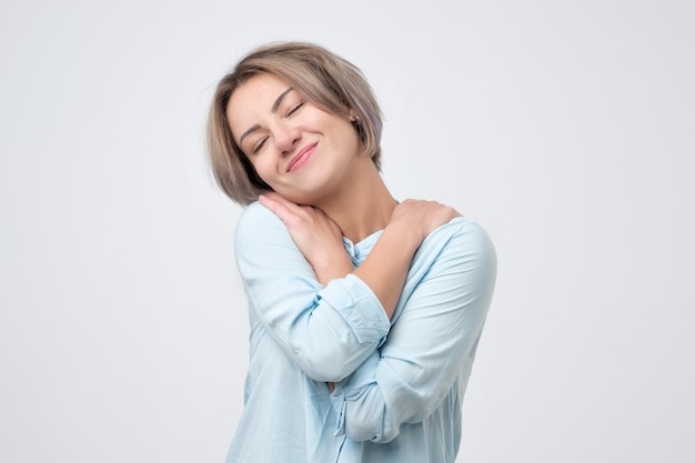 Blanke vrouw in blauw shirt knuffelt zichzelf knuffelend