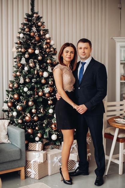 Blanke vrouw in korte jurk poseert voor de camera met haar vriendje in de buurt van de kerstboom