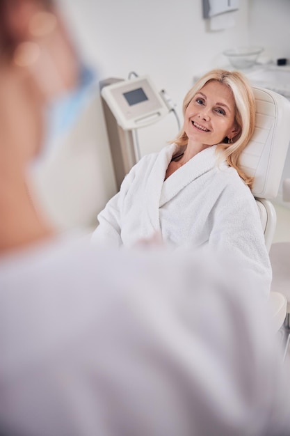 Blanke vrouw in witte pluche badjas die wacht op anti-age huidtherapie in de kamer