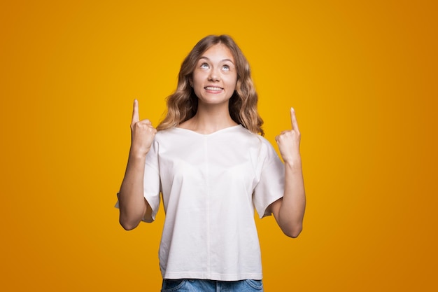 Blanke vrouw in witte t-shirt die naar boven kijkt en wijsvingers omhoog wijst op kopieerruimte geïsoleerd ...