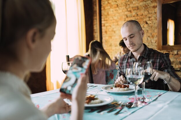 Foto blanke vrouw maakt een foto van haar partner en zijn eten in een restaurant