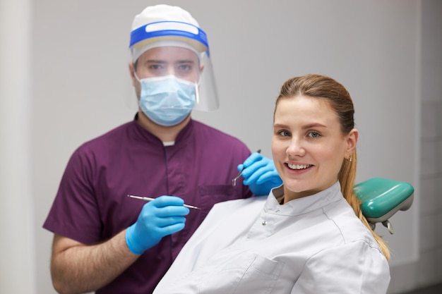 Blanke vrouw met een perfecte glimlach in de tandartspraktijk komt verwende tanden behandelen terwijl ze naar de camera kijkt