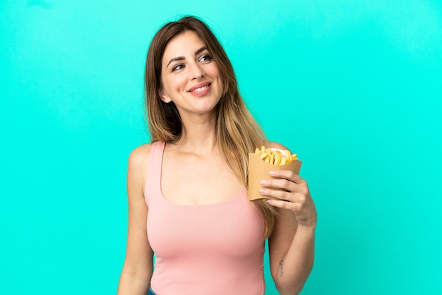 Blanke vrouw met gebakken chips geïsoleerd op een blauwe achtergrond, opzij kijkend en glimlachend