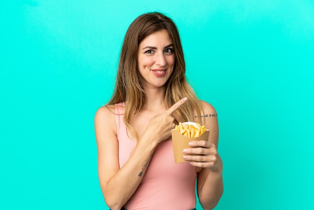 Blanke vrouw met gebakken chips geïsoleerd op een blauwe achtergrond, wijzend naar de zijkant om een product te presenteren