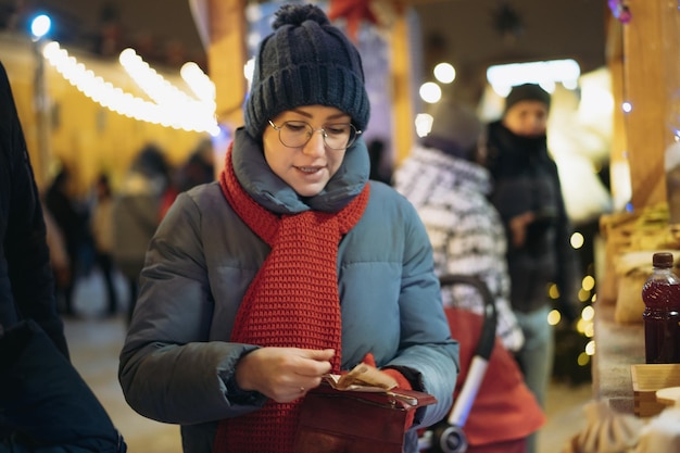 Blanke vrouw met hoed en rode sjaal die snoepjes gaat kopen in de kiosk met contante betaling bij c...