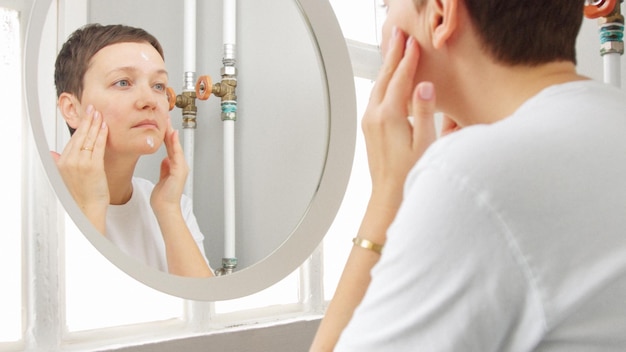 Foto blanke vrouw met kort kapsel voor spiegel in badkamer vol zonlicht