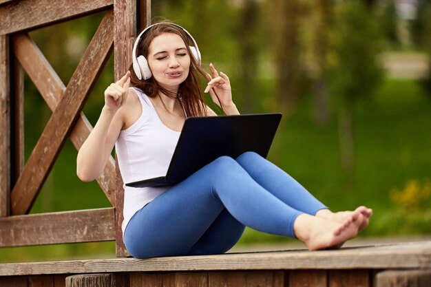 Blanke vrouw met laptop luistert naar muziek via draadloze koptelefoons in openbaar park