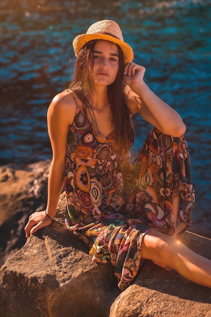 Blanke vrouw met nat haar en een gebloemde jurk en een strohoed aan zee