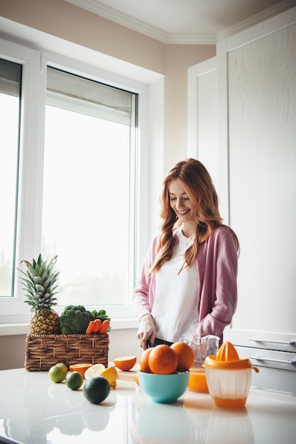 Blanke vrouw met rood haar en sproeten glimlachen tijdens het snijden van fruit voor vers sap