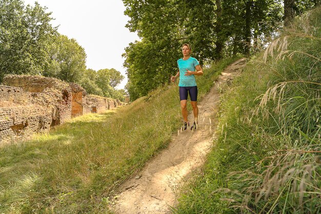 Blanke vrouw met sportief lichaam die in het park bergafwaarts loopt op het platteland tussen de bomen en de prachtige natuur