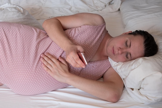 Blanke vrouw met telefoon met weeën op de bank thuis en ademen