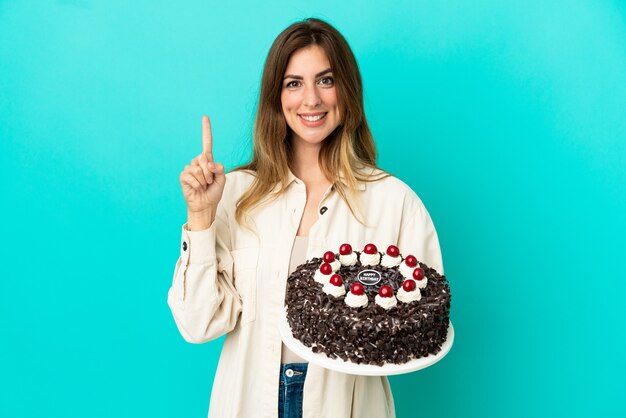 Blanke vrouw met verjaardagstaart geïsoleerd op een blauwe achtergrond die een vinger toont en optilt in teken van de beste