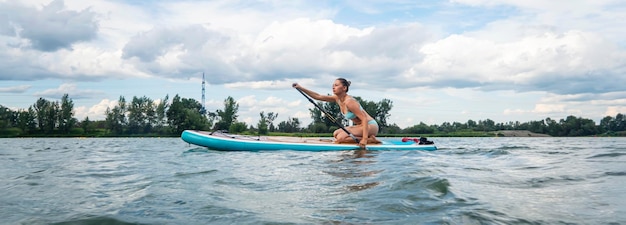 Blanke vrouw rijdt op een sup-bord op de rivier in de stad zomersportpanorama