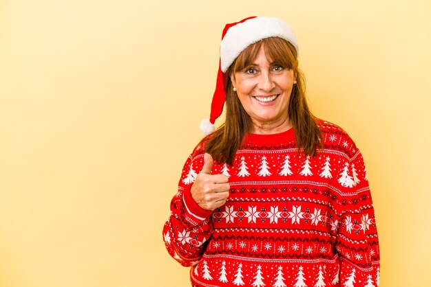 Blanke vrouw van middelbare leeftijd die Kerstmis viert geïsoleerd op gele achtergrond glimlachend en duim omhoog