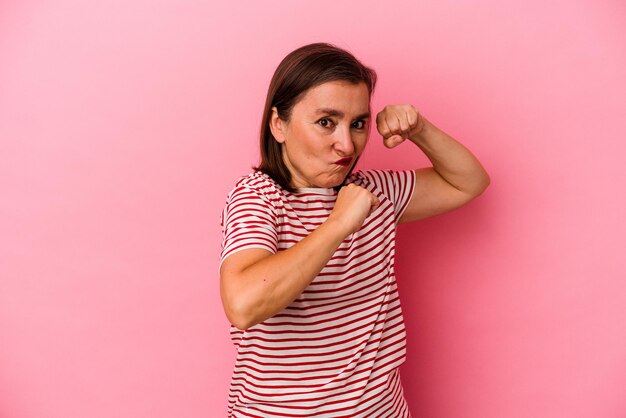 Blanke vrouw van middelbare leeftijd geïsoleerd op roze achtergrond die een vuistslag gooit, woede, vecht vanwege een ruzie, boksen.