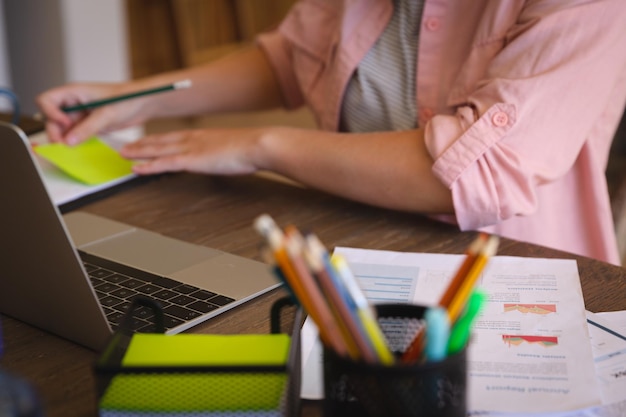 Blanke vrouw zit aan tafel en werkt thuis, gebruikt een laptop en maakt aantekeningen. technologie en communicatie, flexibel thuiswerken.