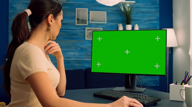 Blanke vrouw zoekt op computer met mock-up groen scherm chroma key-display browsen op internet voor zakelijke communicatie zittend aan bureautafel