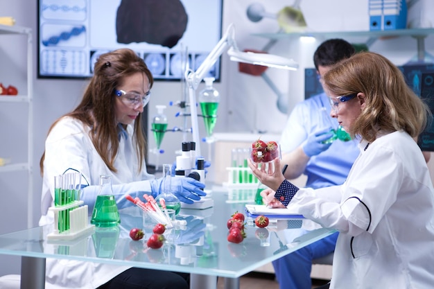 Blanke vrouwelijke wetenschapper die een doos aardbeien vasthoudt na het doen van biologische tests. Microscoop in een laboratoriumonderzoek.