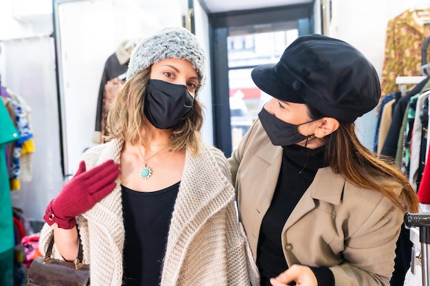 Foto blanke werknemer met een masker uit een kledingwinkel die een klant een juweel voor een spiegel probeert, veiligheidsmaatregelen in de coronaviruspandemie, covid-19