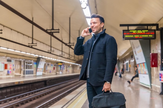 Blanke zakenman van middelbare leeftijd die in de metro wacht tot de trein naar zijn werk gaat, pratend aan de telefoon