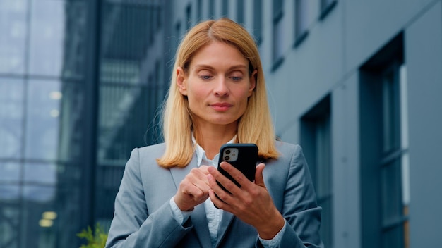 Blanke zakenvrouw die telefoon buiten vasthoudt vrouw met smartphone scrollend scherm werk online