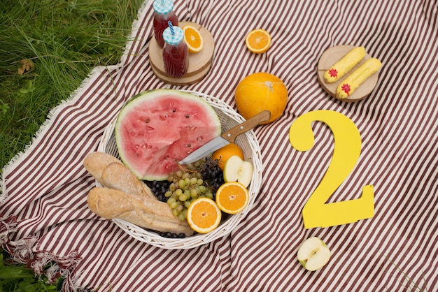 A blanket and a basket with fruit and watermelon in the park in summer, on a sunny day