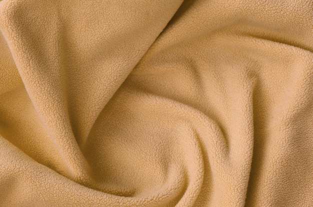 The blanket of furry orange fleece fabric. A background of light orange soft plush fleece material with a lot of relief folds