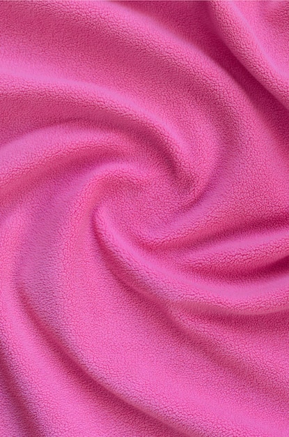 毛皮のようなピンクのフリース生地の毛布。レリーフのひだがたくさんあるライトピンクの柔らかい豪華なフリース素材の背景