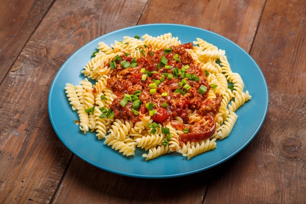 Blauw bord met bolognese pasta op een houten tafel bestrooid met uien